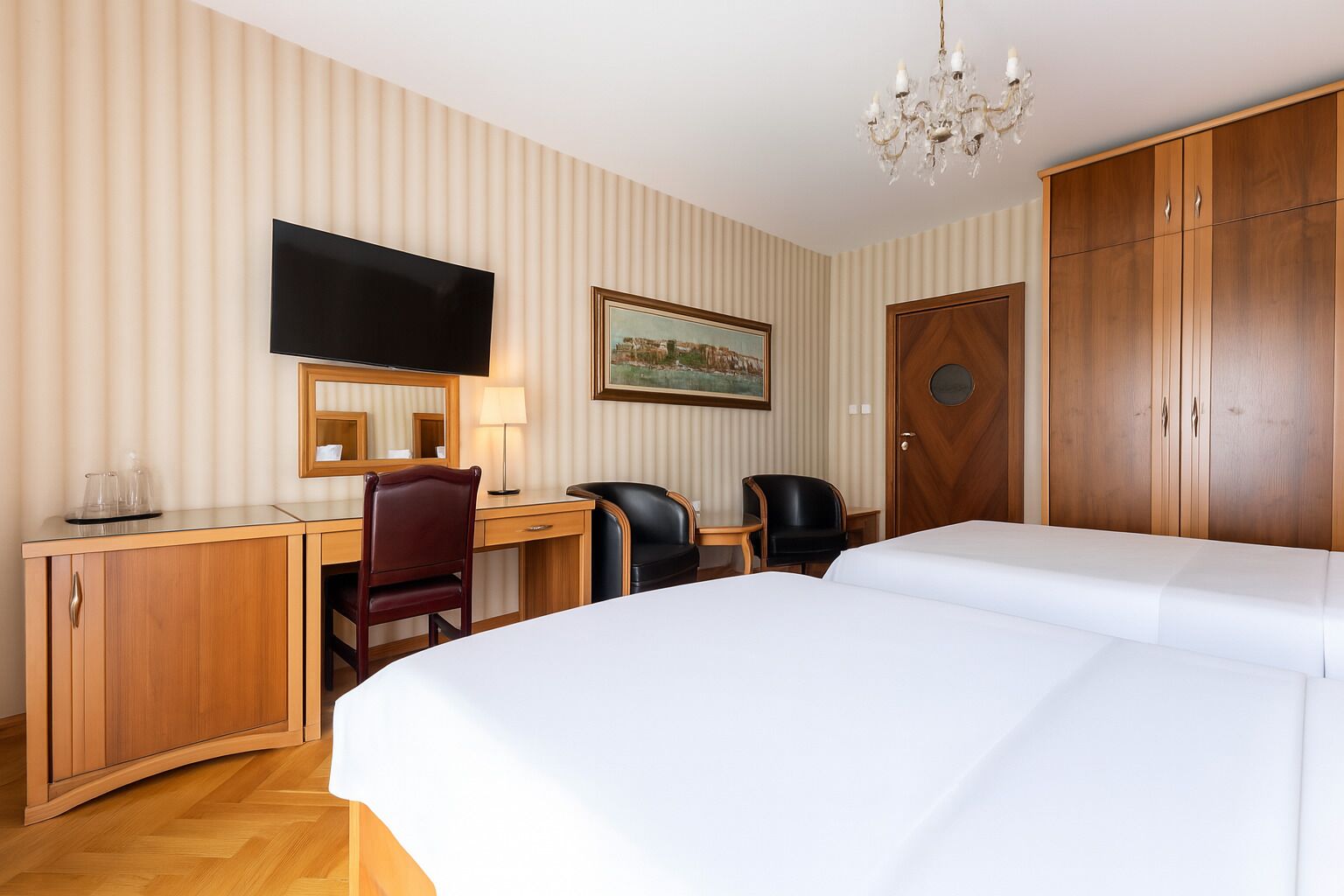 Hotelkamer met een bed, bureau, stoelen, televisie, een kroonluchter en een kledingkast.