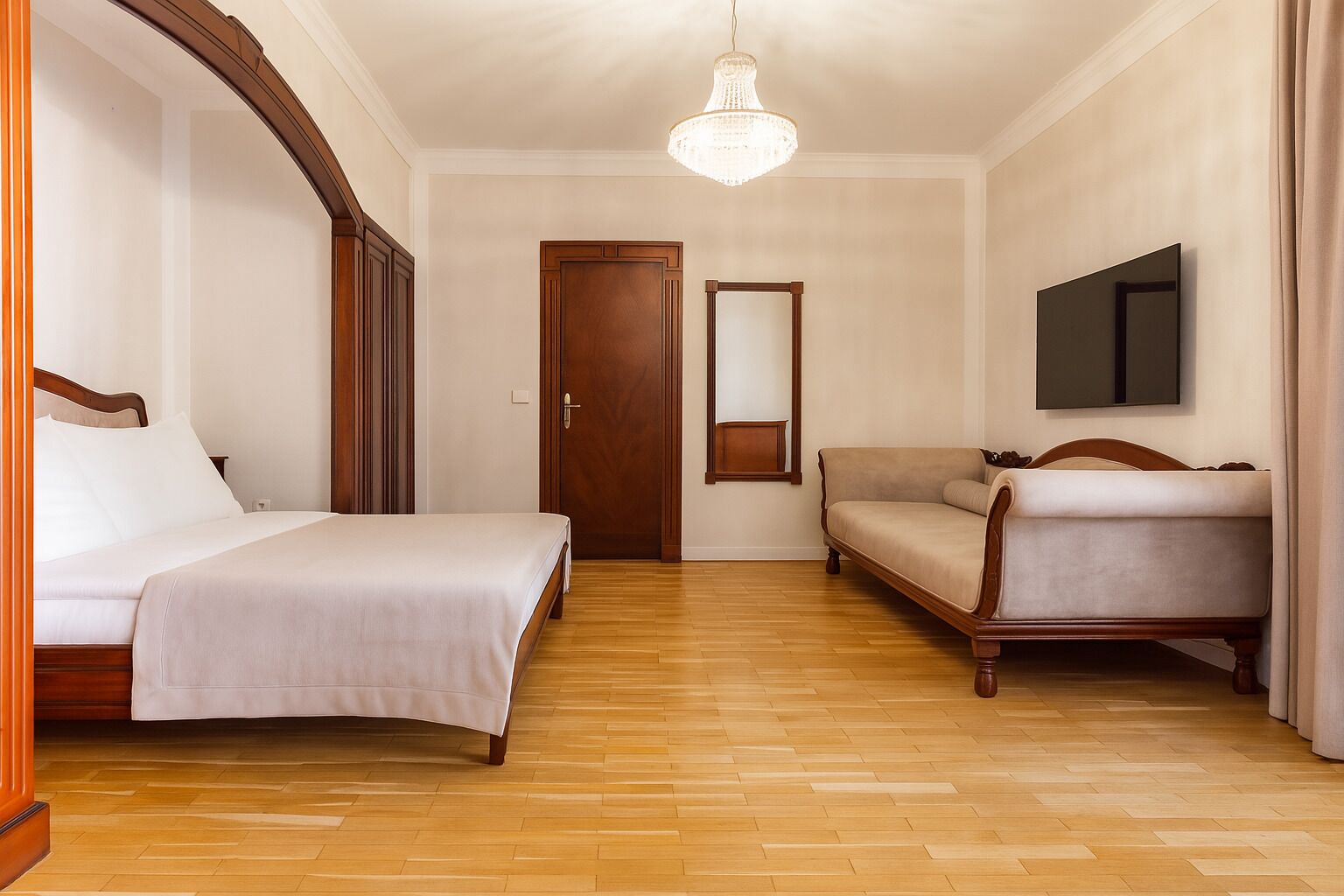 Una habitación de hotel con cama, sofá, suelo de madera, candelabro y espejo.