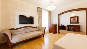 A hotel room with a wooden floor, a sofa, a bed, a desk, and a television mounted on the wall.
