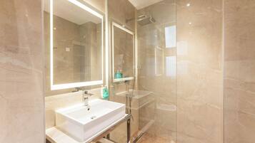 A modern bathroom with a glass-enclosed shower, a white sink, and a large mirror.
