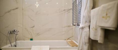 Un baño con pared de azulejos de mármol, una bañera blanca y un perchero con una toalla blanca.