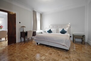 A bedroom with a large bed, a desk, a chair, and a small table.