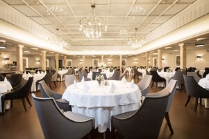 Un salón de banquetes con mesas redondas, sillas grises y candelabros.