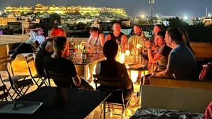 A group of people seated around a table with drinks, overlooking a cityscape with illuminated buildings at night. - Hotel Pol Haveli (Jaisalmer)