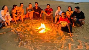 A group of people sitting around a campfire on a sandy beach at dusk. - Hotel Pol Haveli (Jaisalmer)