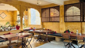 A restaurant with wooden tables and chairs, a high ceiling, and decorative arches. - Hotel Pol Haveli (Jaisalmer)