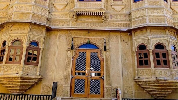 A traditional building with ornate architecture, featuring multiple arched windows and a central entrance with a metal grill. - Hotel Pol Haveli (Jaisalmer)