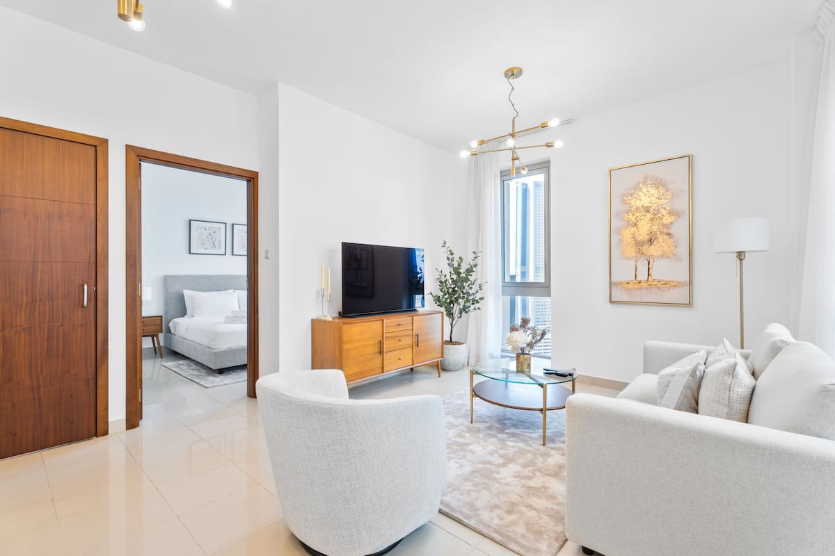 A modern living room with a sofa, a coffee table, and a TV. There is a wooden cabinet and a plant on the windowsill.