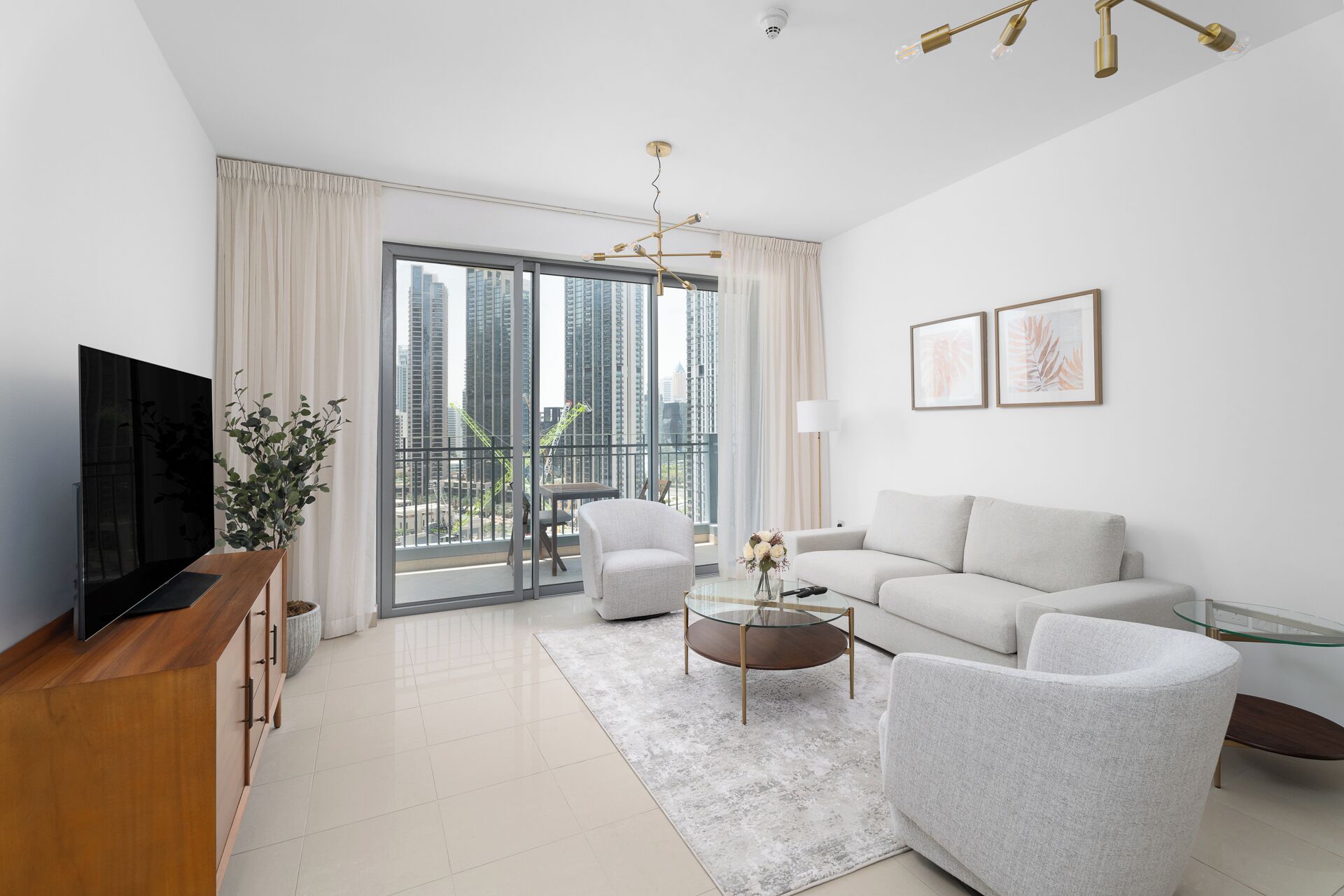 Una sala de estar moderna con un televisor de pantalla plana, un sofá, una silla, una mesa de centro de vidrio y un balcón con vistas a la ciudad.
