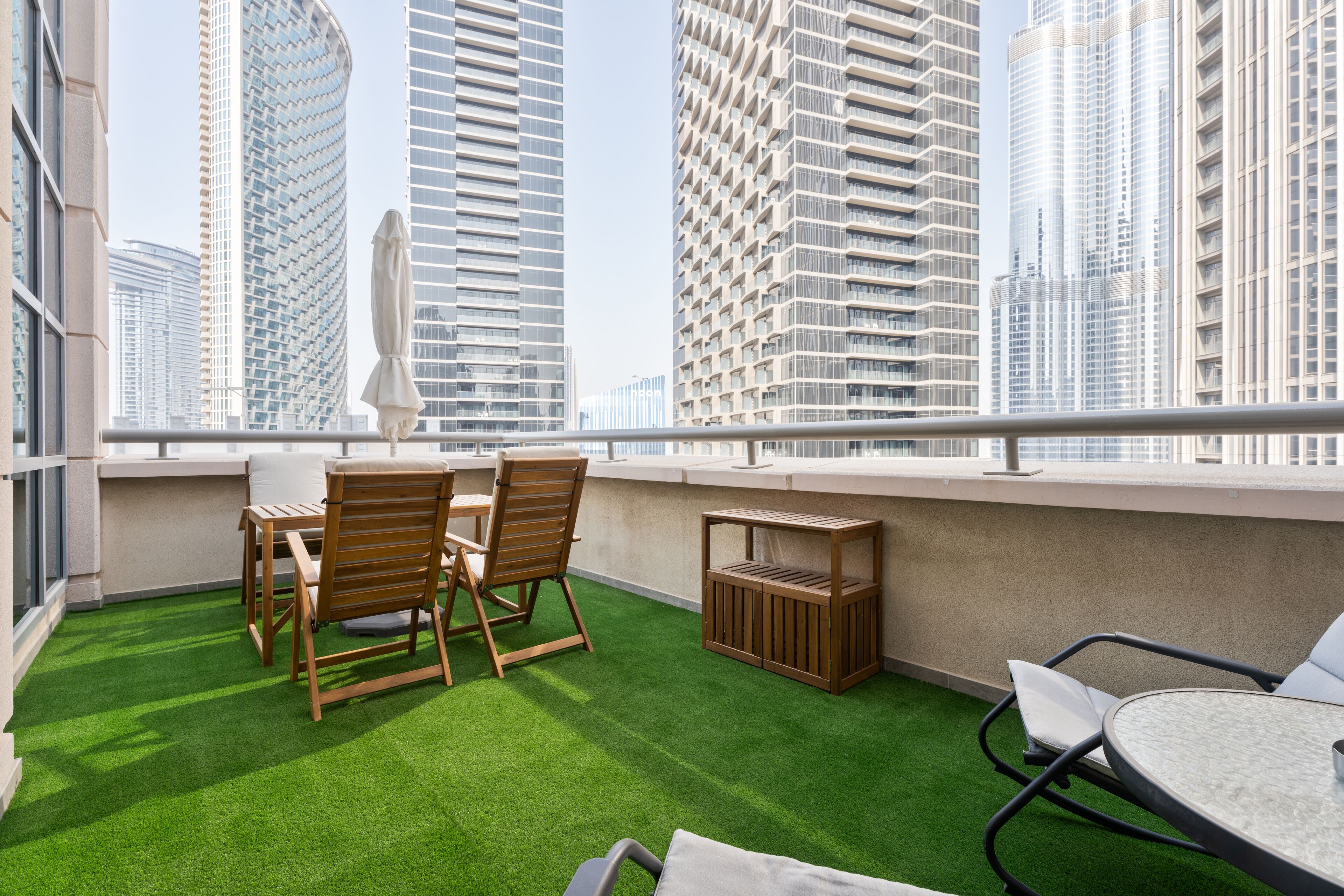 Une terrasse sur le toit, dotée d’un revêtement d’herbe artificielle, de mobilier en bois et offrant une vue sur les immeubles modernes.