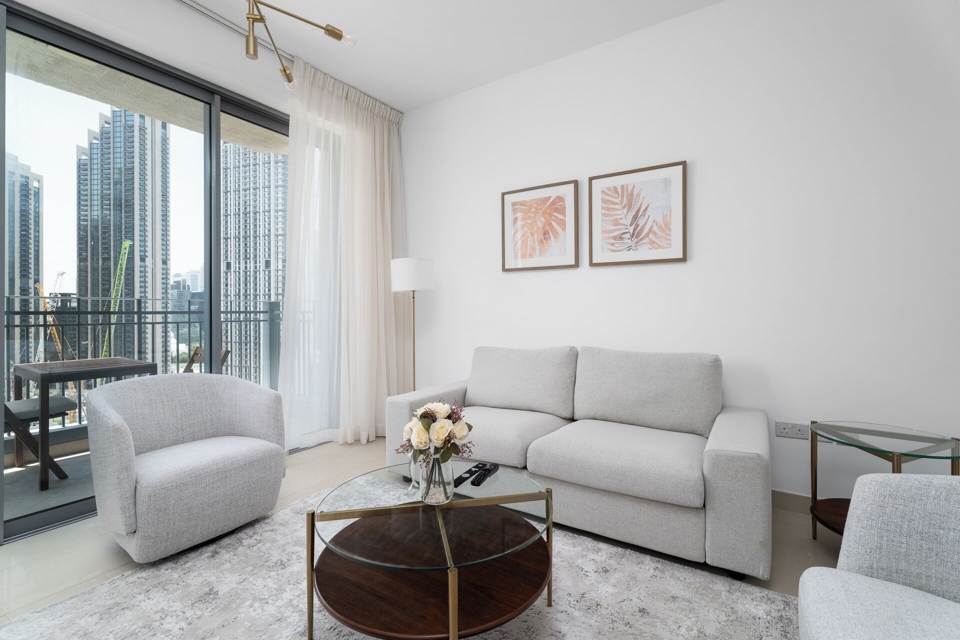 A modern living room with a grey sofa, two armchairs, a glass coffee table, and artwork on the wall.