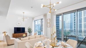Una sala de estar moderna con una mesa de vidrio dispuesta para una comida, un sofá y una televisión al fondo.