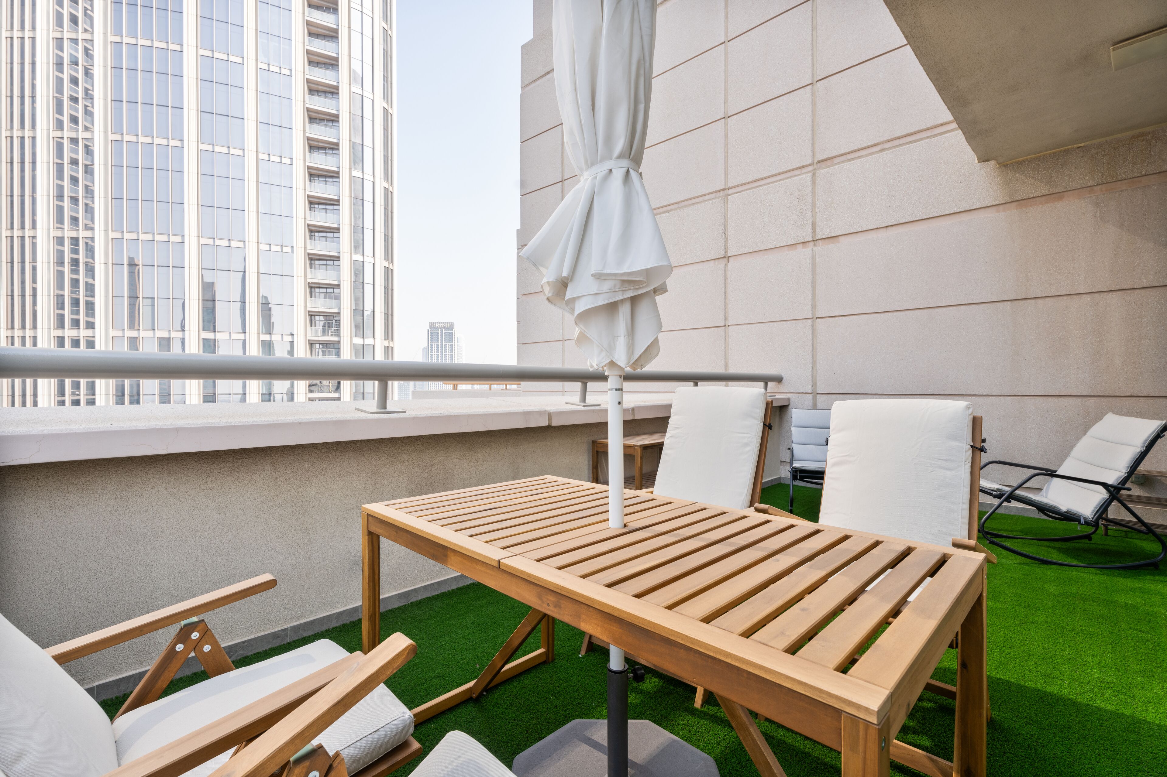 A balcony with a wooden table, white chairs, and a white umbrella.