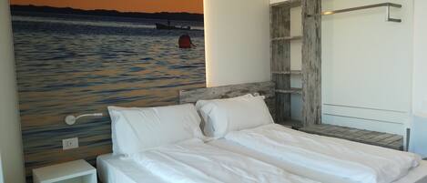 Ein Schlafzimmer mit einem Bett, einem Nachttisch, einem Holzkopfteil und einem Wandbild eines Bootes auf dem Wasser.