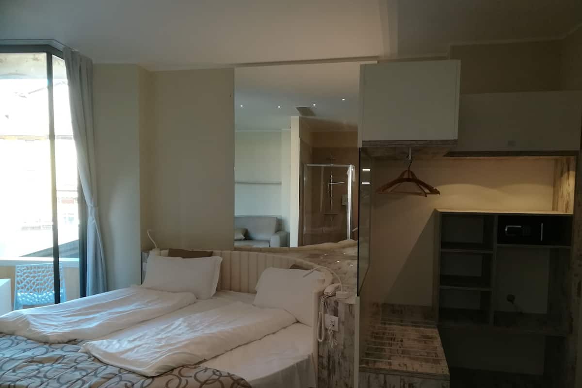 Ein Hotelzimmer mit Bett, Spiegel, Kleiderschrank und einem durch eine Glastür sichtbaren Badezimmer.