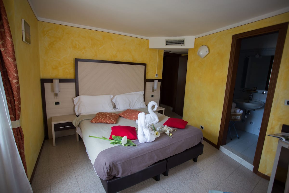 Ein Hotelzimmer mit Bett, Nachttisch, einem durchgegangene Tür sichtbaren Badezimmer und einem kleinen Tisch mit Lampe.