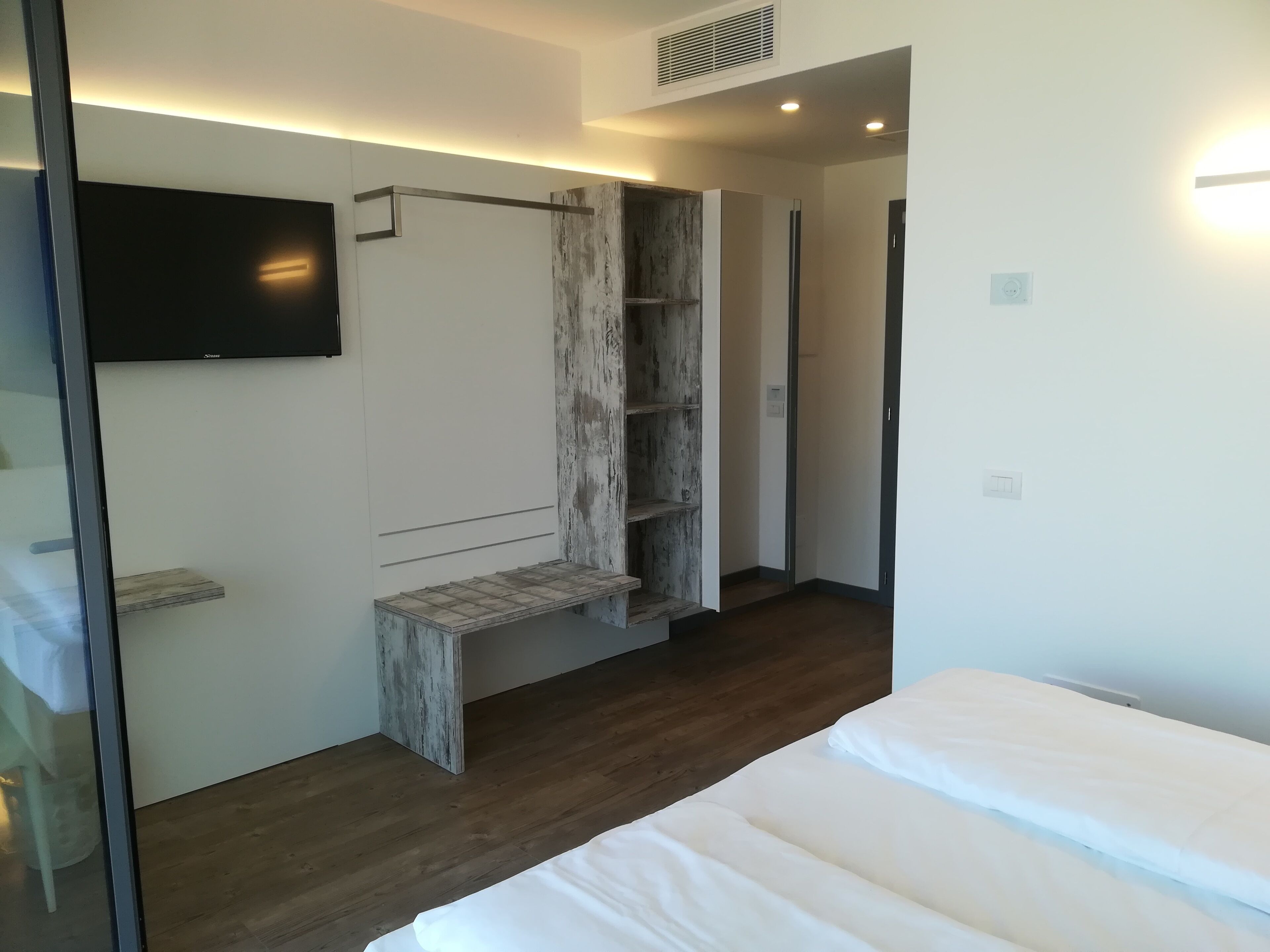 A modern bedroom with a wooden floor, a bed with white bedding, a built-in wardrobe, and a mounted TV.