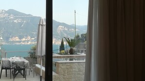 A terrace with a table and chairs, a stone wall, and a view of mountains and the sea. - Hotel San Marco (Torri del Benaco)