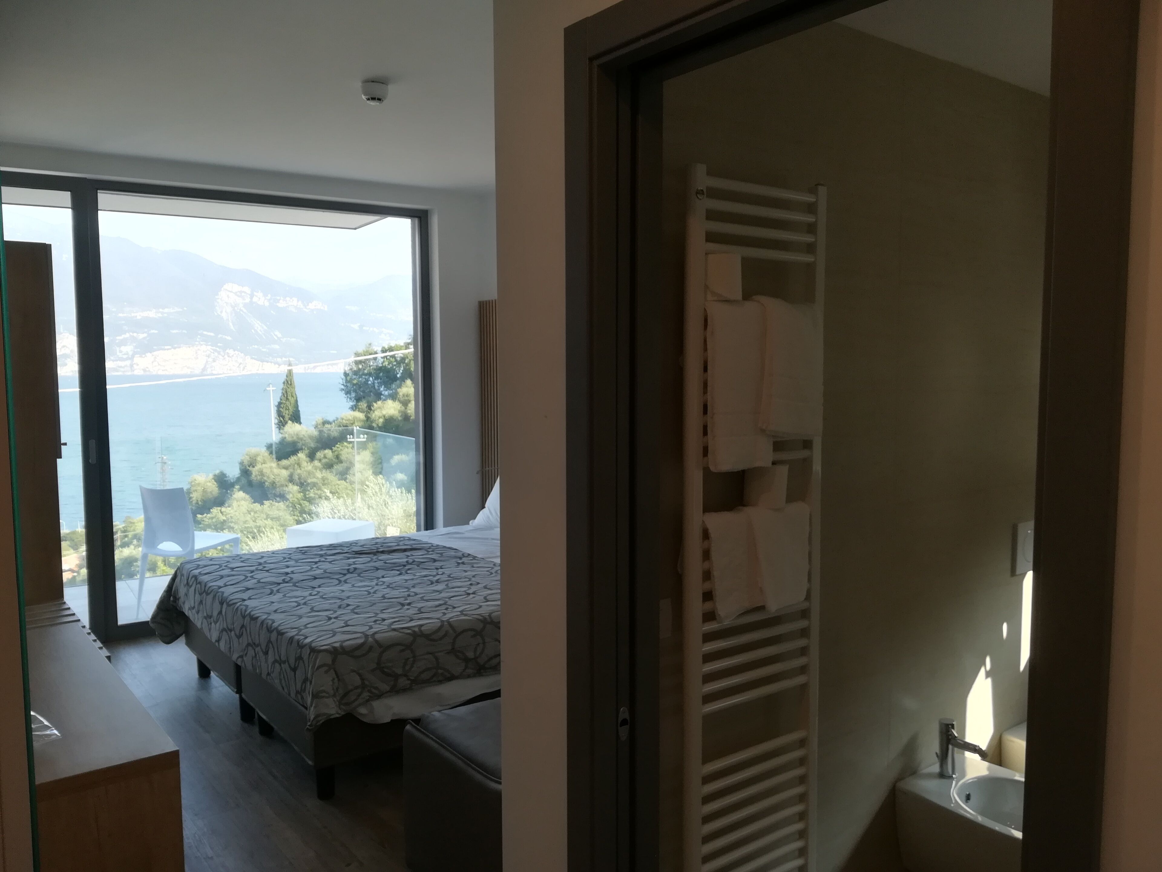 A bedroom with a bed, a bedside table, and a view of a body of water and mountains.