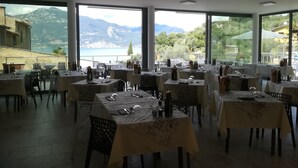 A restaurant with multiple tables, each set with cutlery and wine glasses, overlooking a scenic mountain and lake view. - Hotel San Marco (Torri del Benaco)