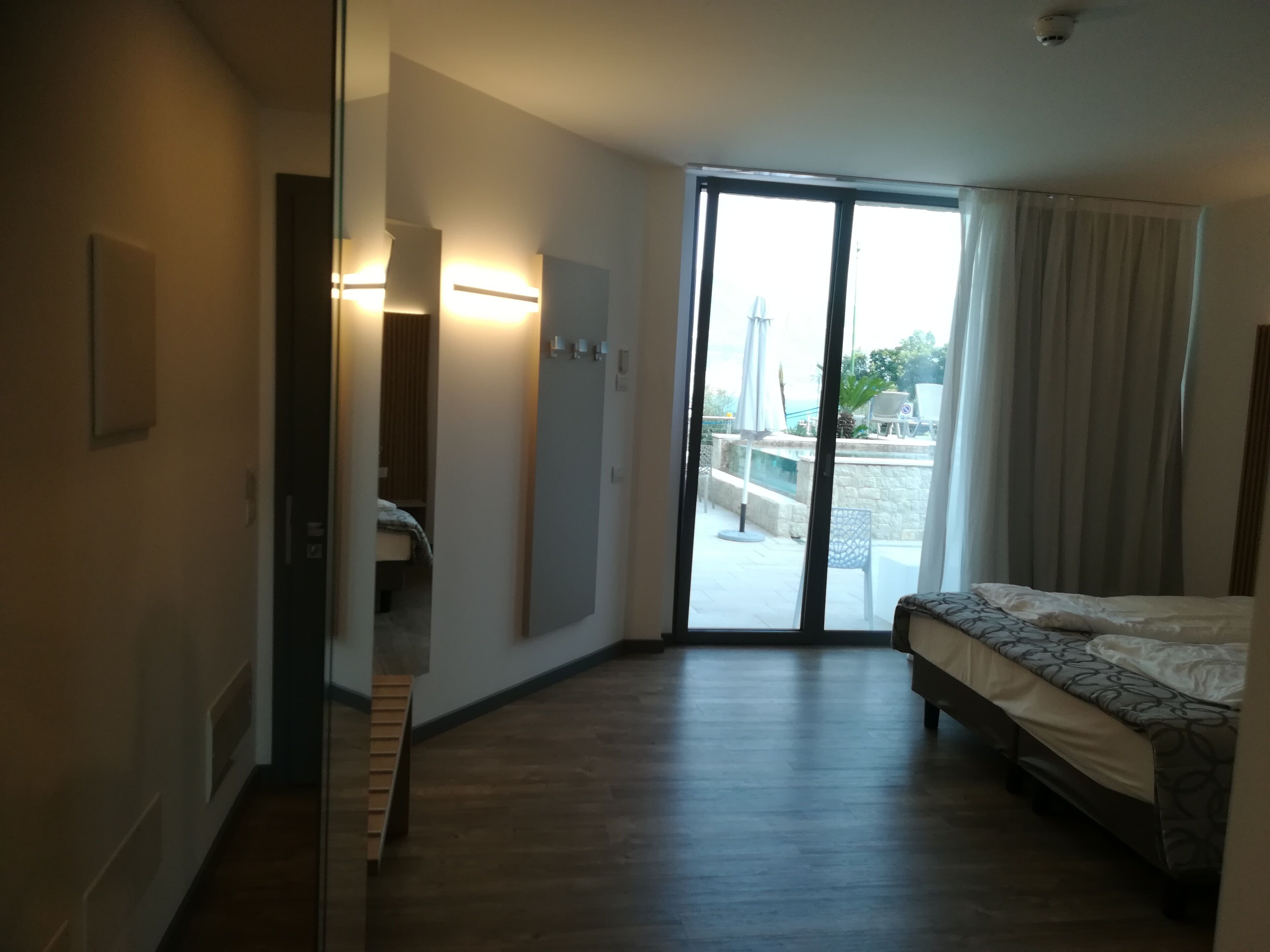 Ein Hotelzimmer mit Bett, Bad und einer Glasschiebetür, die auf einen Balkon mit Pool und Gartenmöbeln führt.