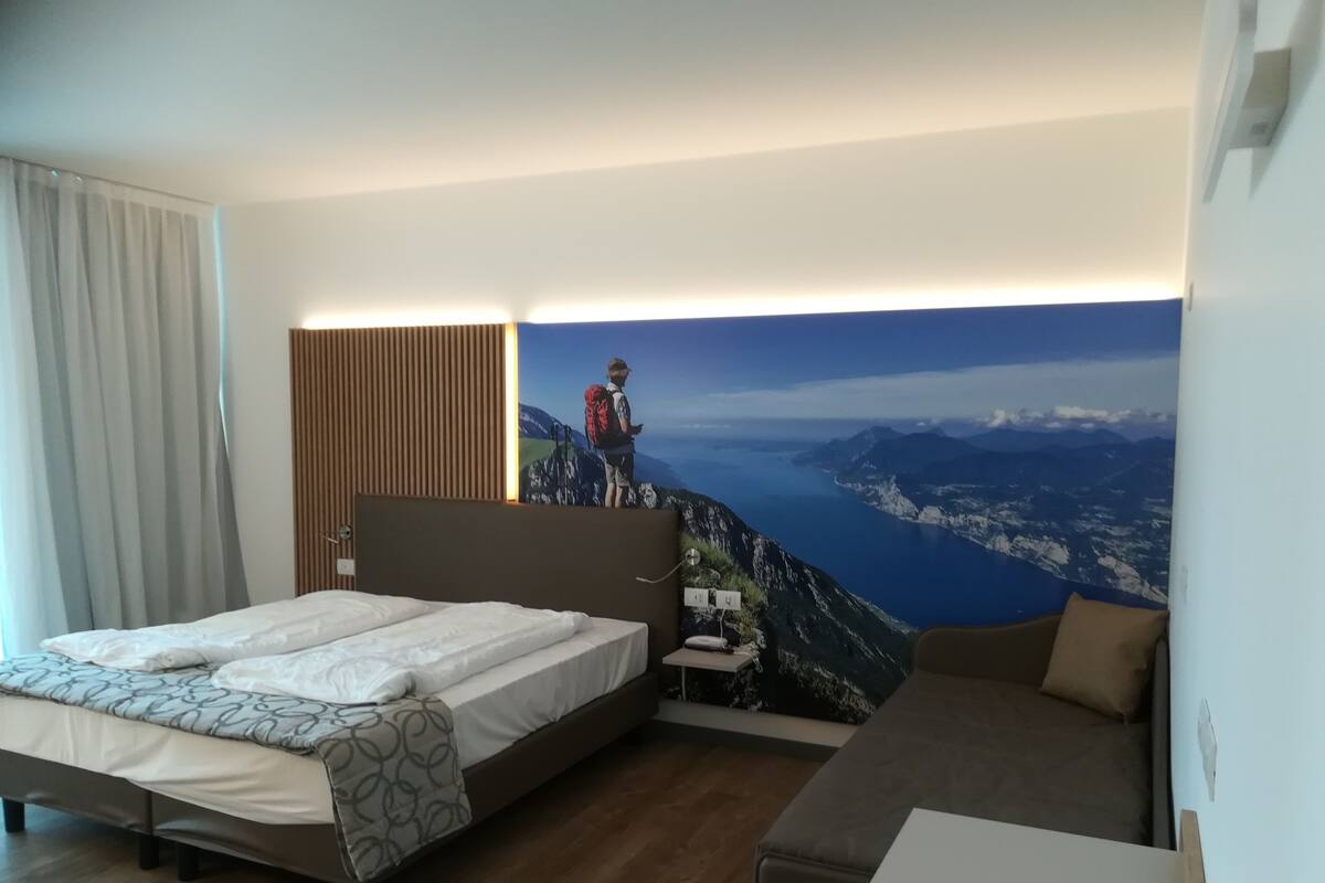 Ein Schlafzimmer mit Bett, einer Couch, einem Schreibtisch und einer großen Wandmalerei von einem Wanderer auf einem Berggipfel.