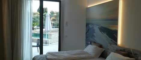 Habitación de hotel con cama, un cuadro en la pared y vistas a un área exterior con piscina y sombrillas.