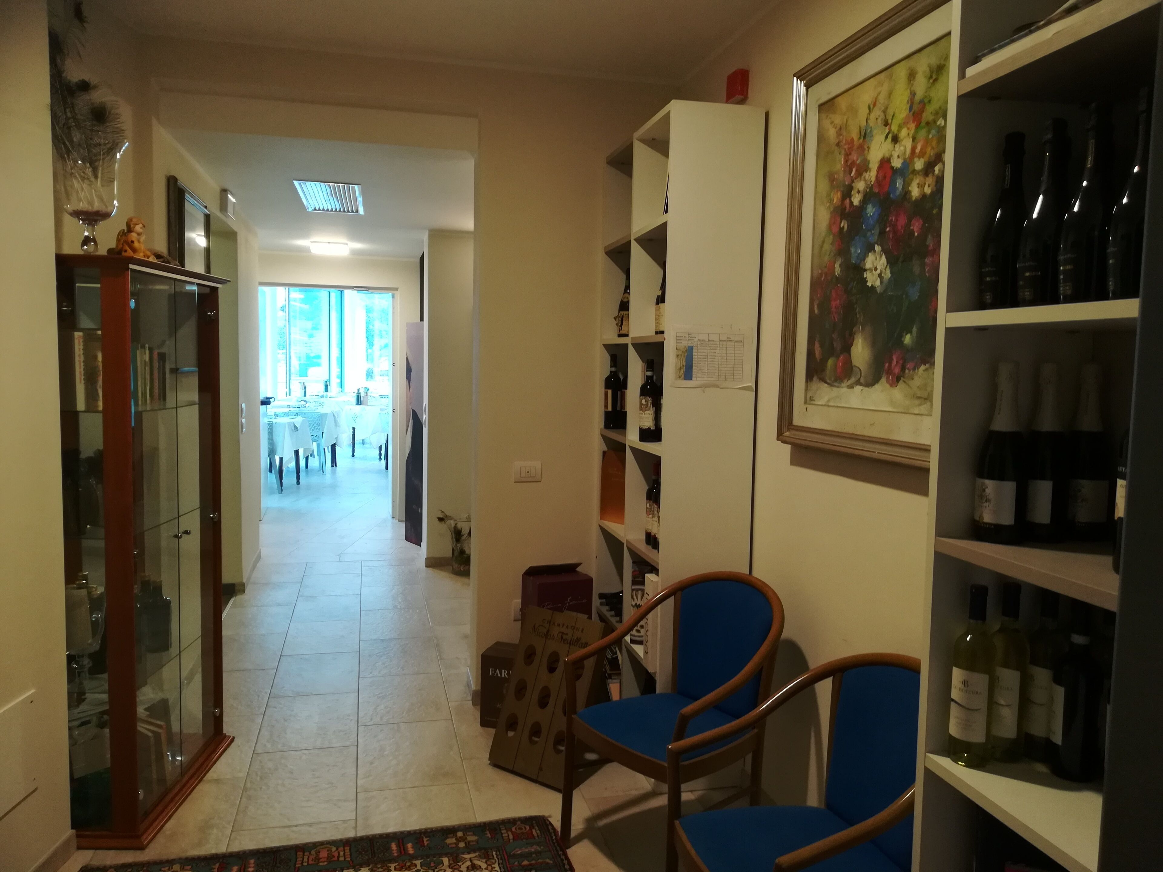 A hallway with a glass cabinet, a blue chair, and a wine rack.