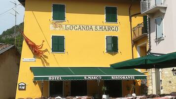Ein gelbes Gebäude mit der Aufschrift „Hotel S. Marco“ und „Ristorante“, das ein Restaurant kennzeichnet. Vor dem Gebäude befinden sich Tische und Stühle im Freien.