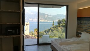 A bedroom with a large sliding glass door leading to a balcony with a scenic view of mountains and a body of water. - Hotel San Marco (Torri del Benaco)