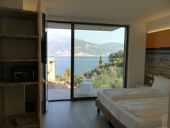 Un dormitorio con un gran ventanal corredizo que da a un balcón con vistas panorámicas de montañas y una masa de agua.