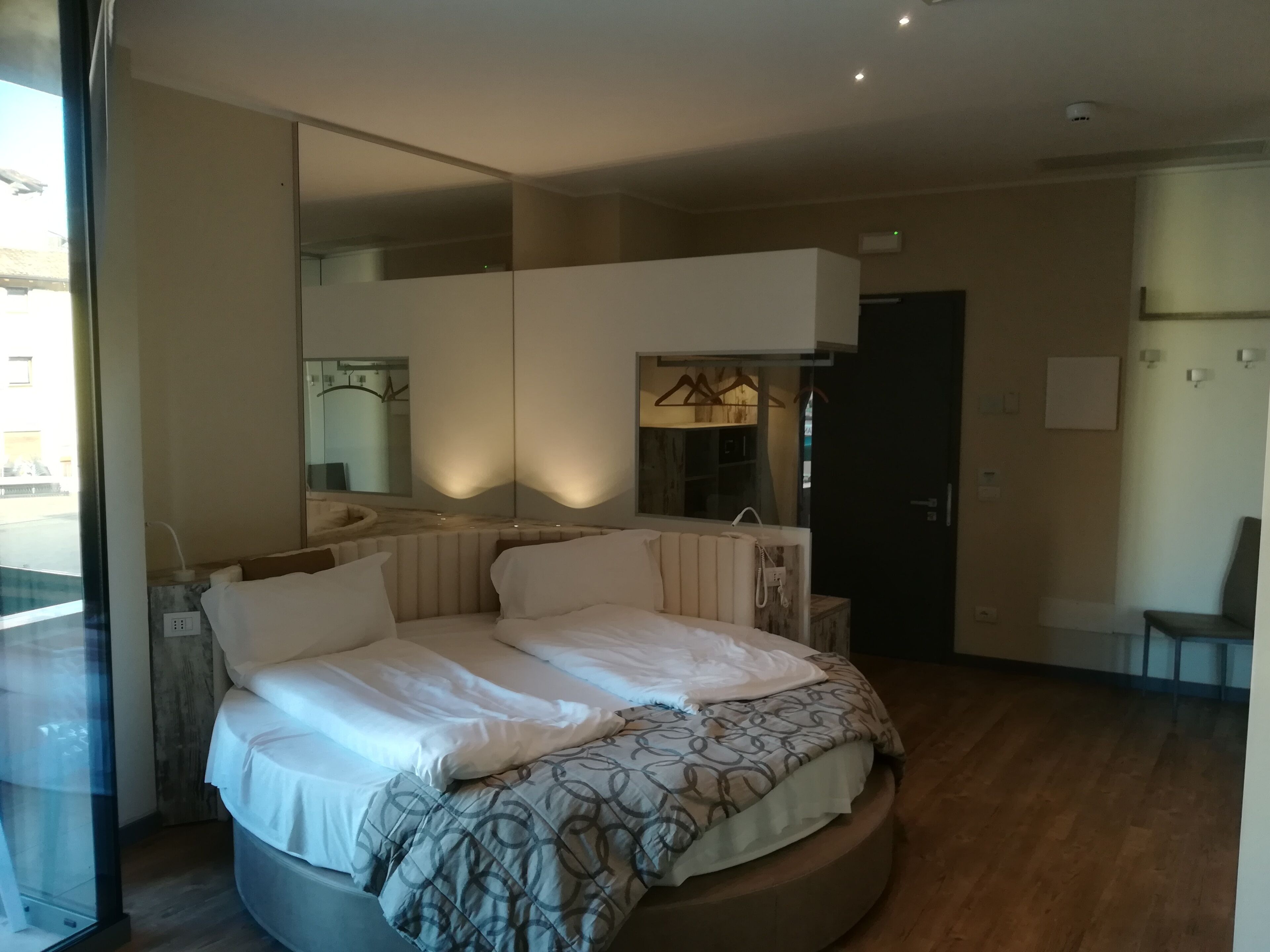 A modern bedroom with a curved bed, a large mirror, and a wooden floor.