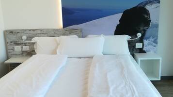 Una cama bien hecha con sábanas blancas en una habitación con un gran mural en la pared que muestra un paisaje montañoso.