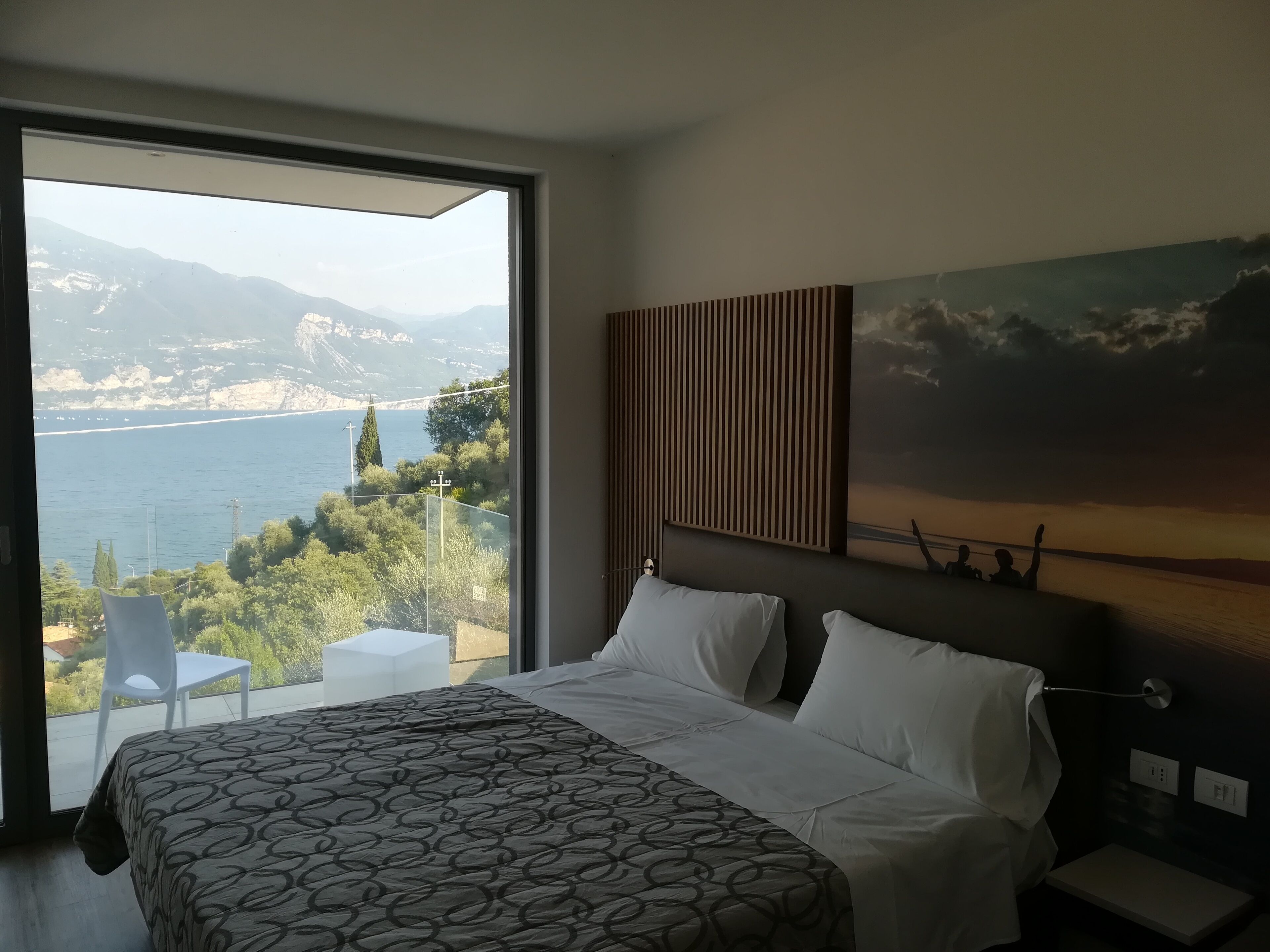 A bedroom with a large bed, a view of the sea, and a painting on the wall.