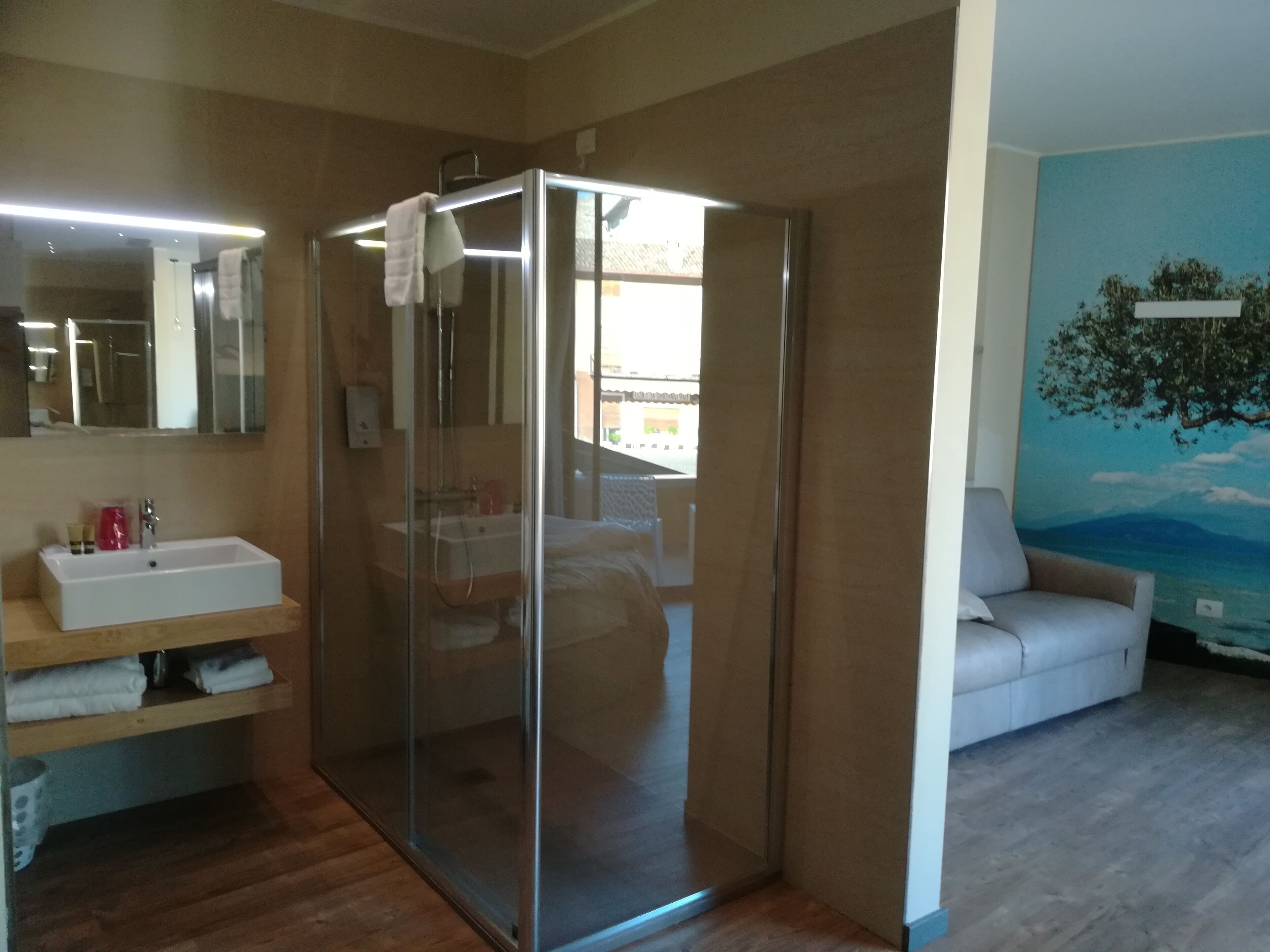 A bathroom with a glass-enclosed shower, a sink with toiletries, and a mirror.