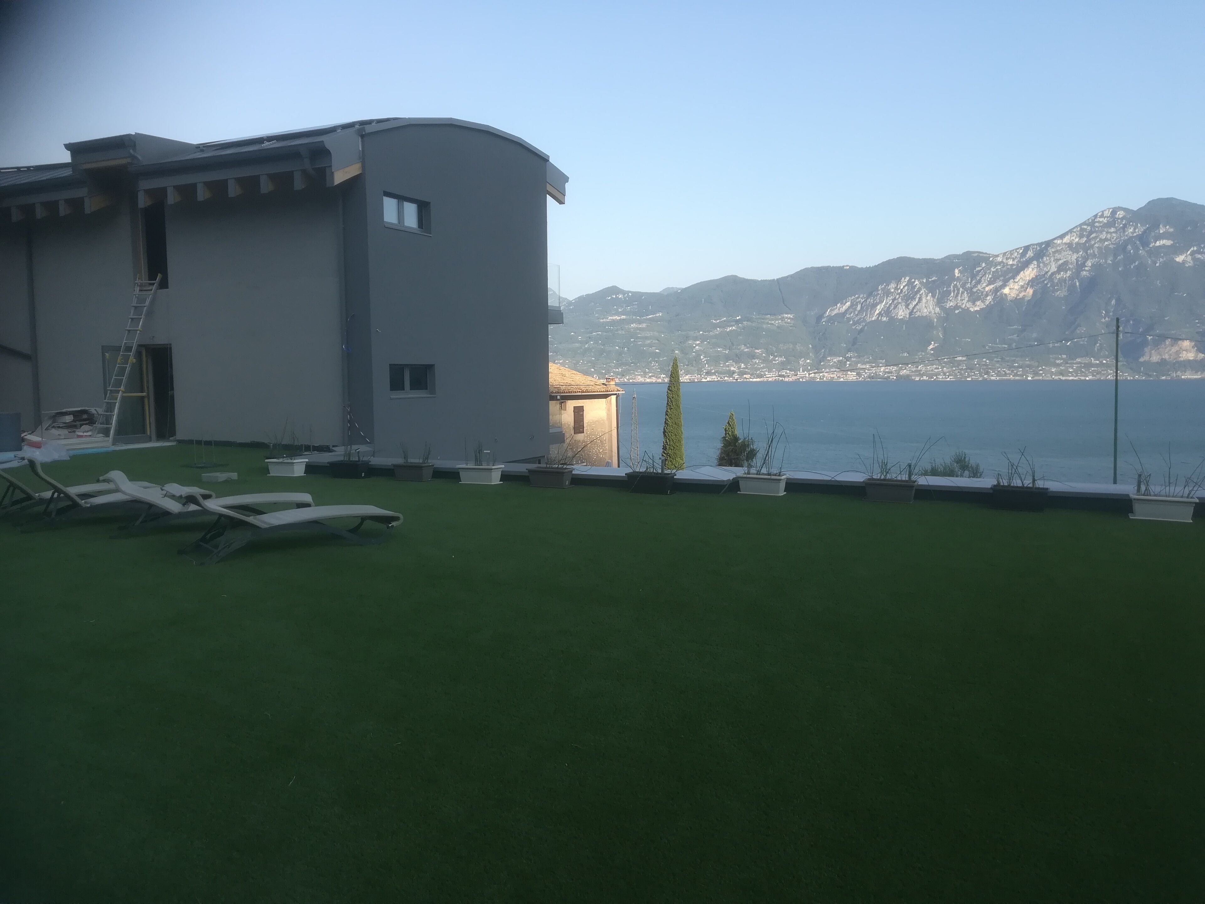 Un edificio moderno con fachada curva, un pequeño balcón y vistas al agua y montañas al fondo.
