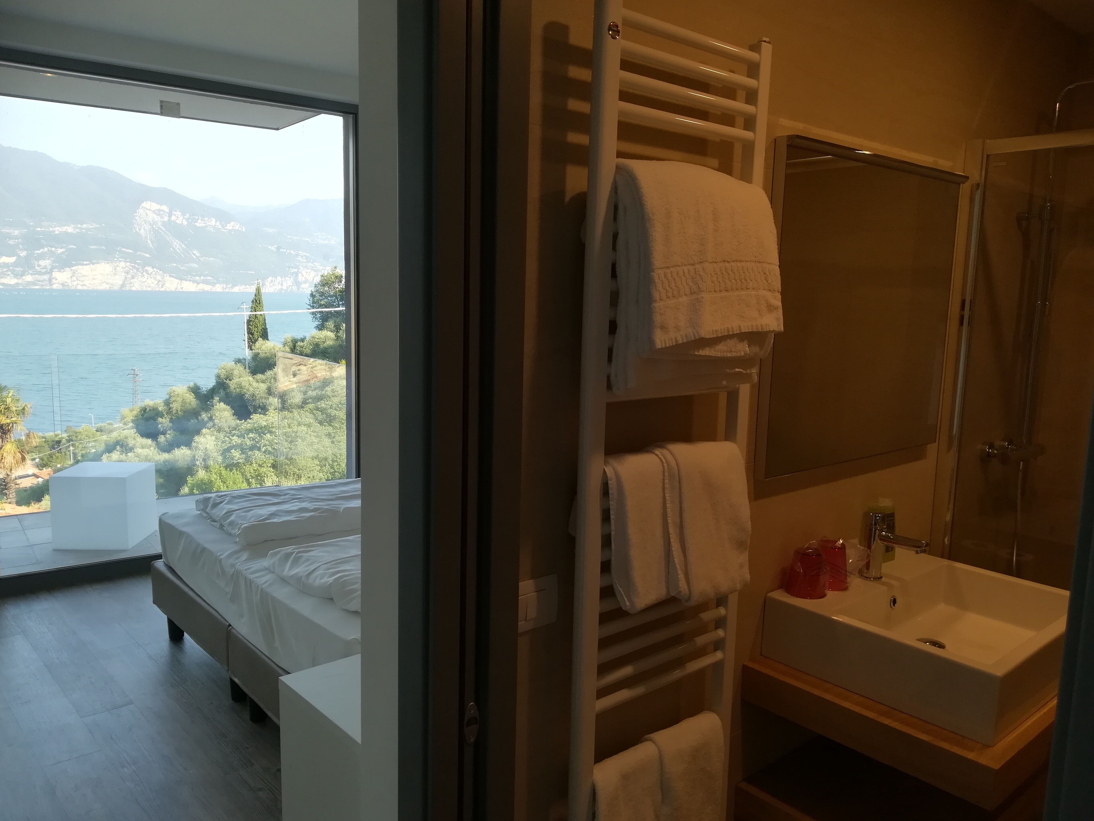 Um quarto com cama, um banheiro com pia e espelho, e vista para um lago e montanhas.