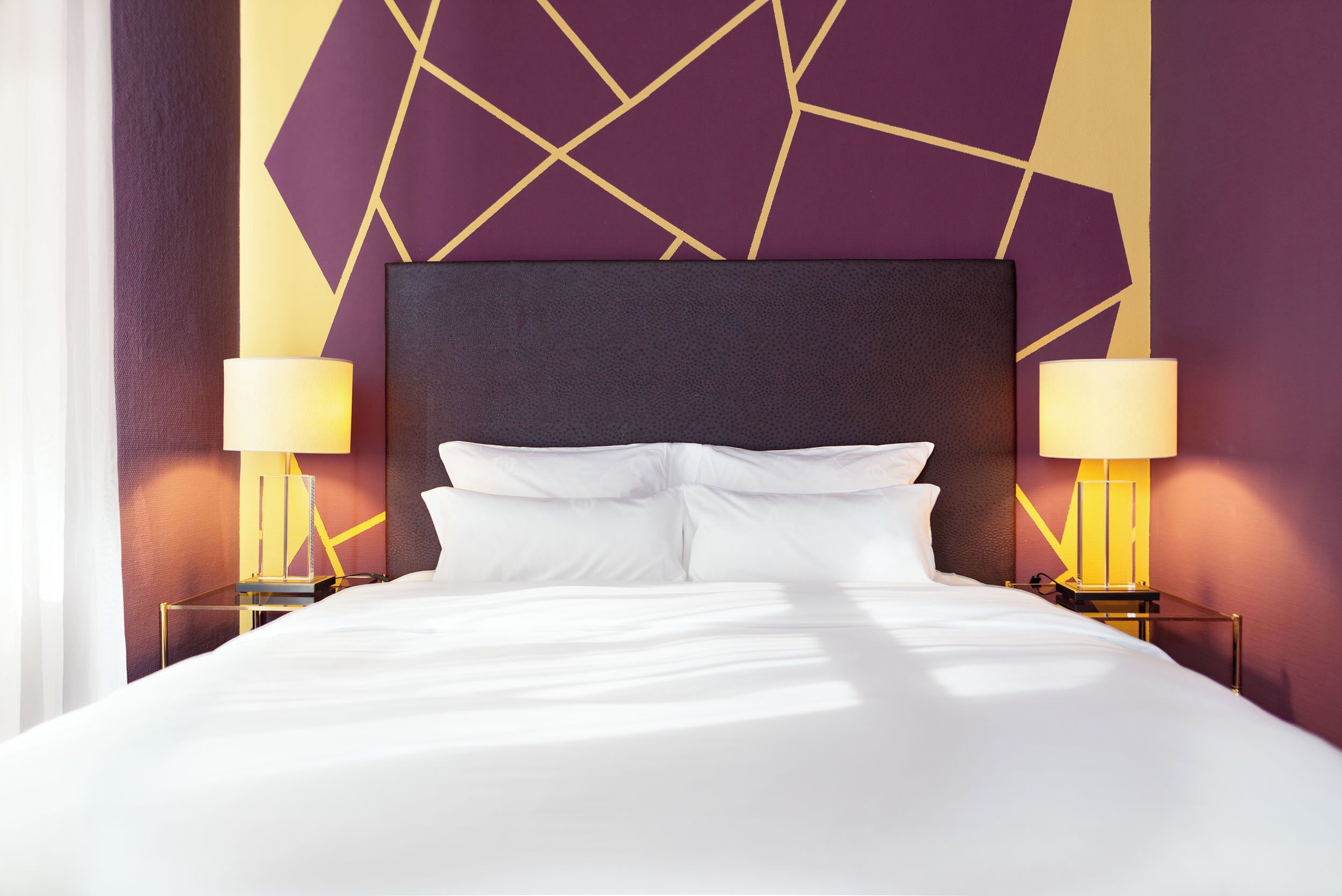 Una habitación de hotel con una cama grande, dos mesitas de noche con lámparas y una pared con estampado geométrico.