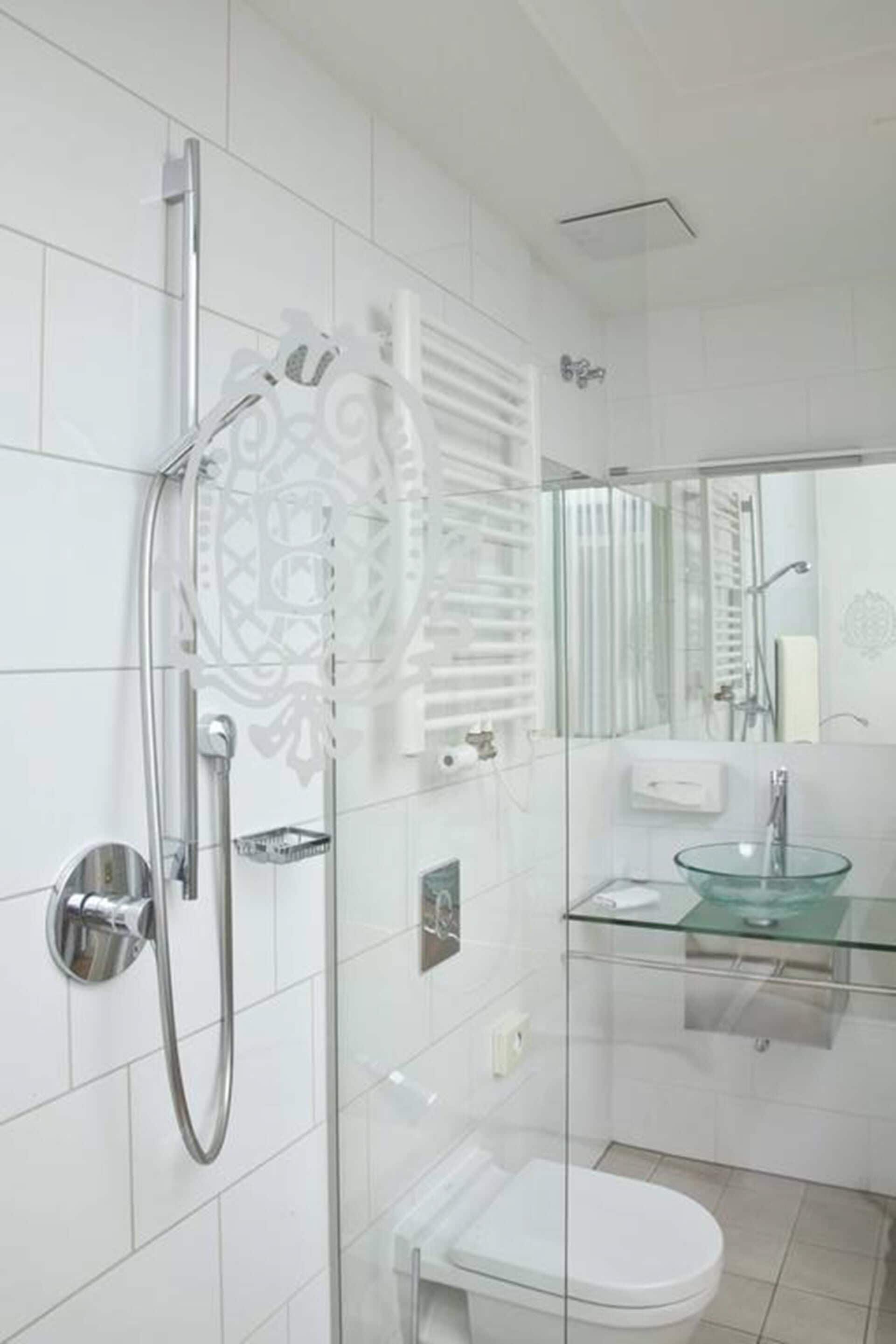 Un baño moderno con cabina de ducha de vidrio, lavamanos de vidrio y váter blanco.
