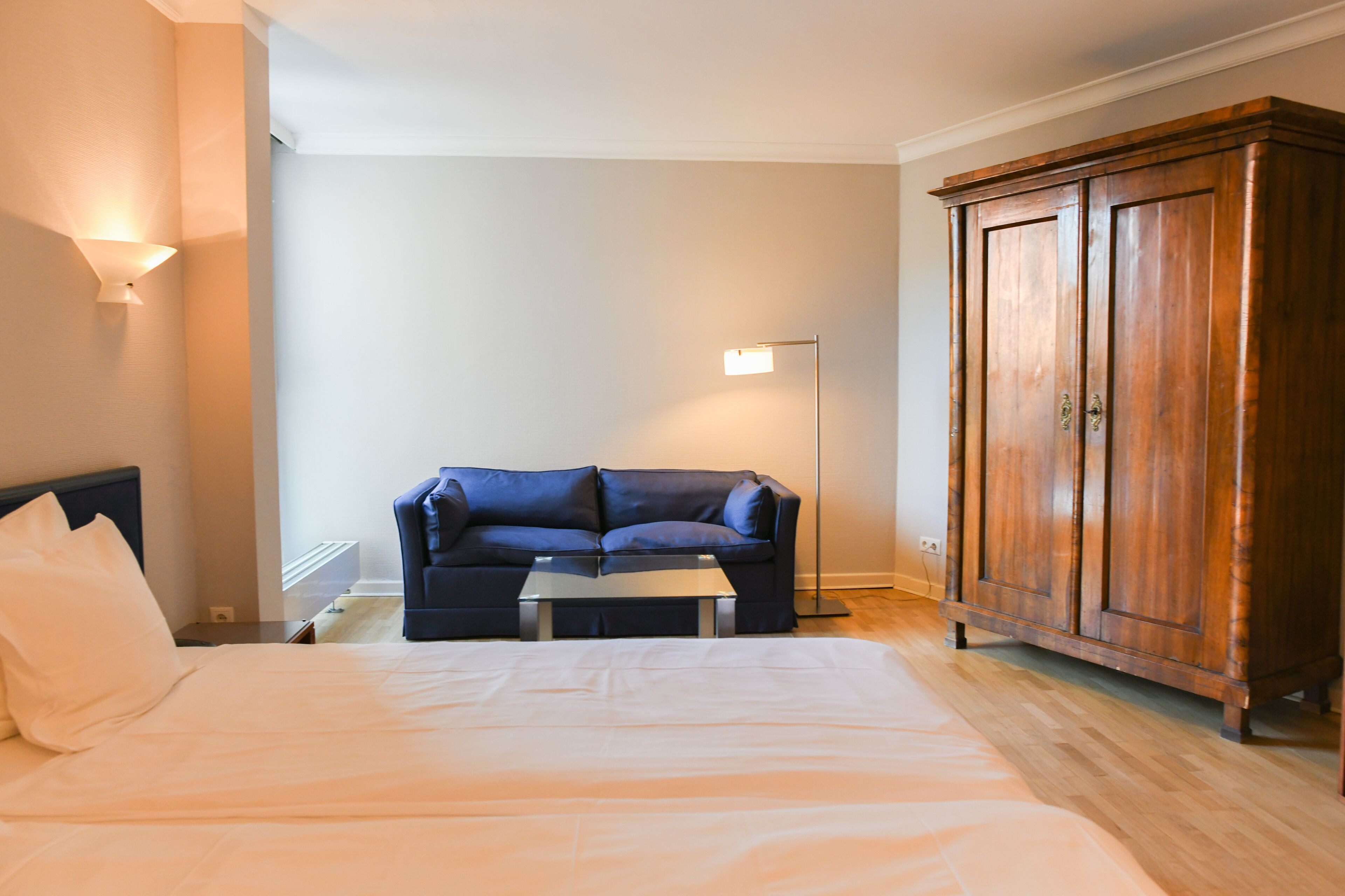 Een slaapkamer met een bed, een blauwe bank, een houten garderobe en een vloerlamp.