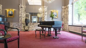A grand room with a grand piano, marble columns, and a red carpeted floor.