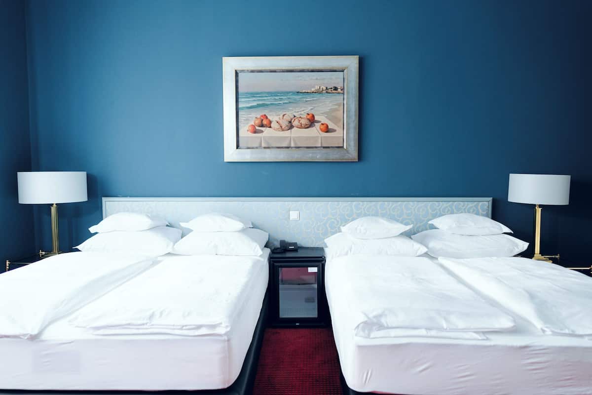 Quarto de hotel com duas camas, um quadro representando uma cena de praia e um tapete vermelho.