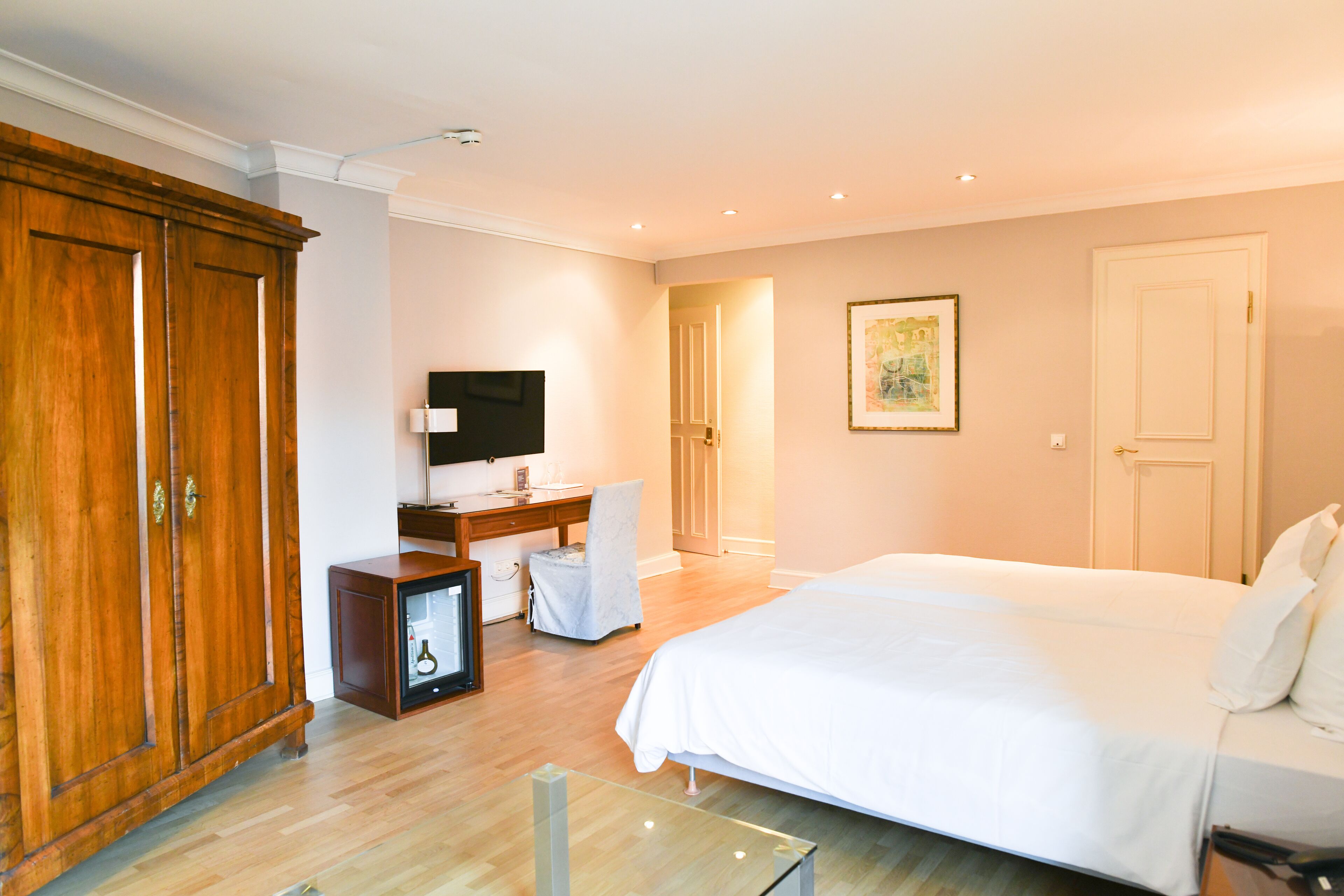 A hotel room with a large bed, a desk with a chair, a television, and a wardrobe.