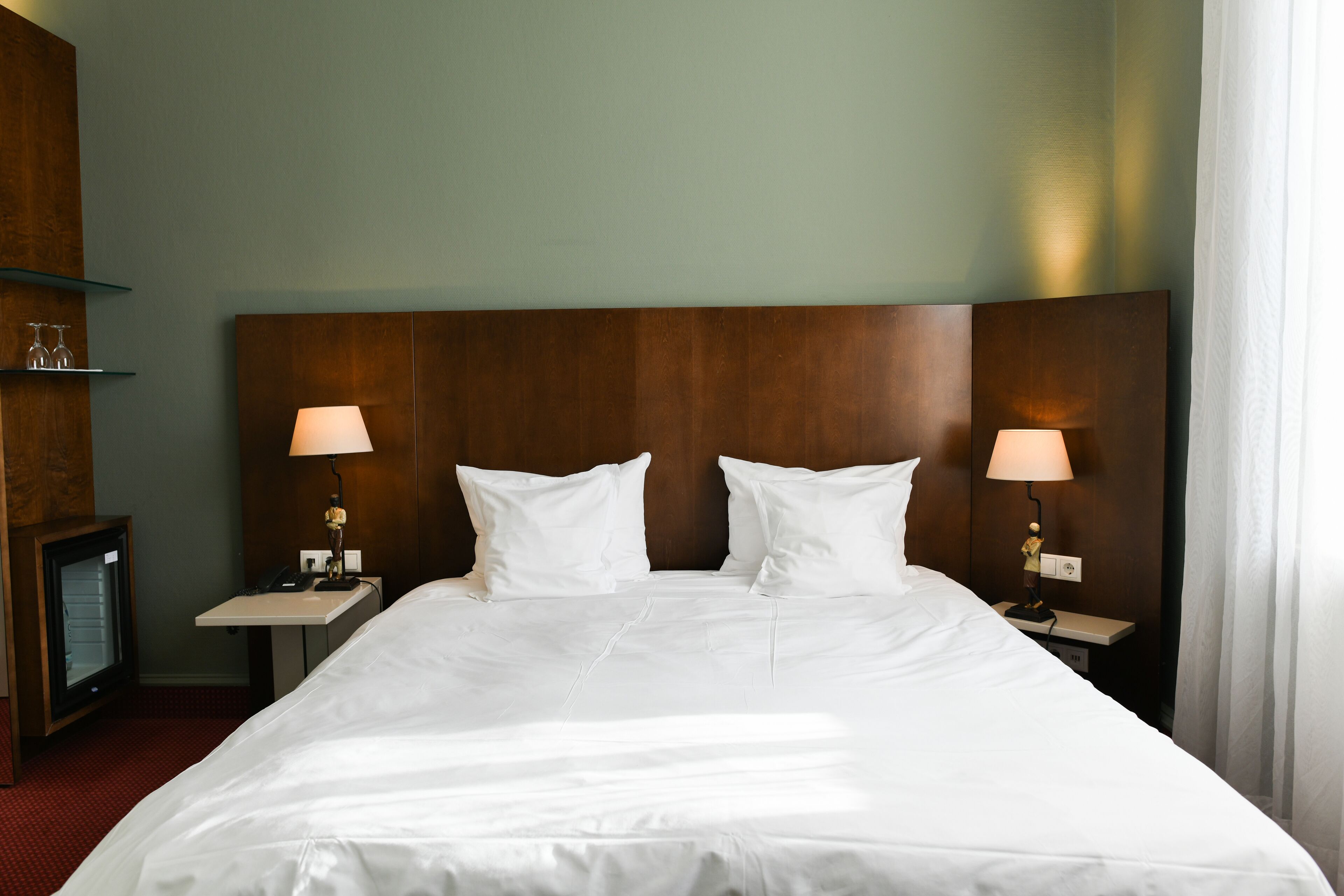 Habitación de hotel con una cama grande, dos mesitas de noche con lámparas, un escritorio pequeño con teléfono y un televisor a la izquierda.