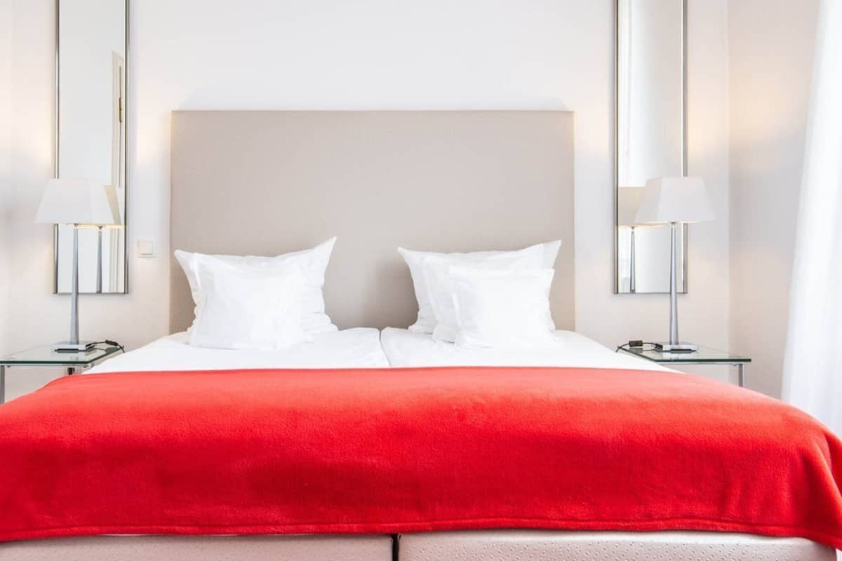 Quarto de hotel com uma cama grande, duas mesas de cabeceira e duas luminárias na parede.