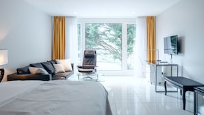 A modern hotel room with a bed, a sofa, a chair, a desk, and a TV.