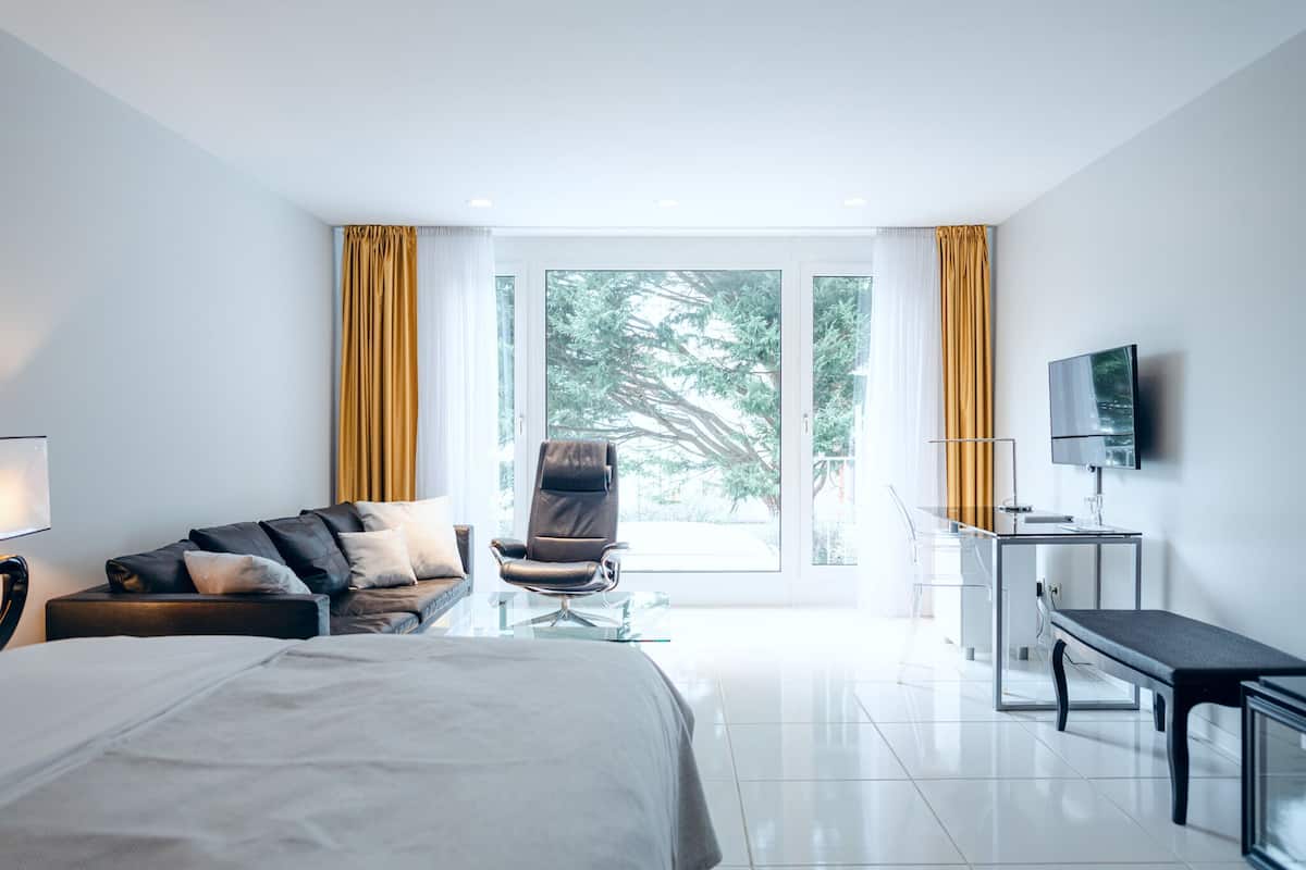 Quarto de hotel moderno com cama, sofá, poltrona, escrivaninha e televisão.