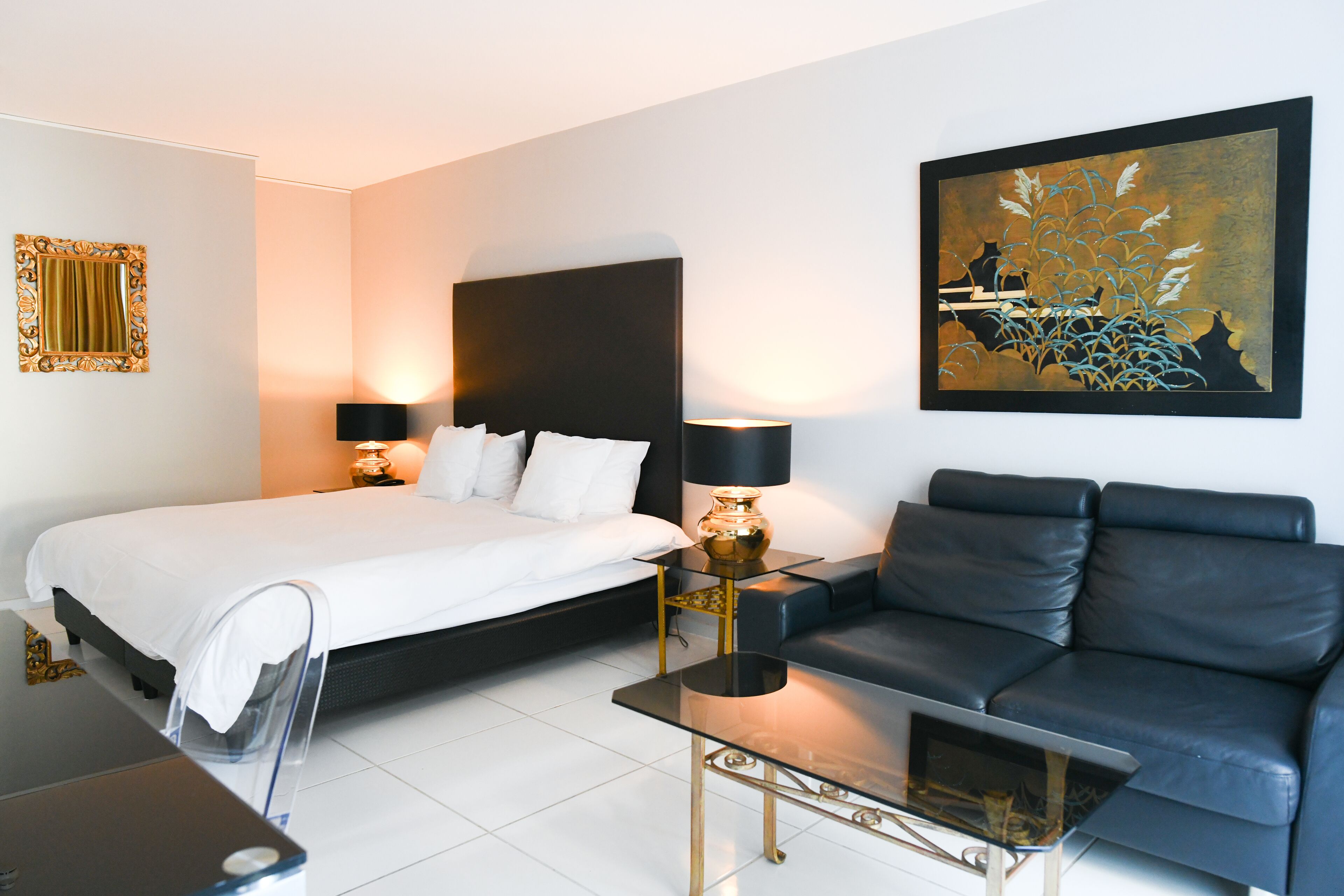 A modern hotel room with a bed, a sofa, a coffee table, and a painting on the wall.