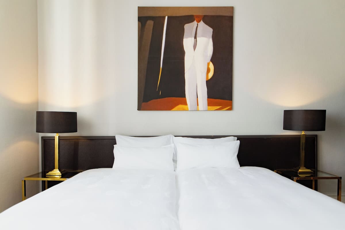 Quarto de hotel com uma cama grande, duas mesas de cabeceira com abajures e um quadro na parede.