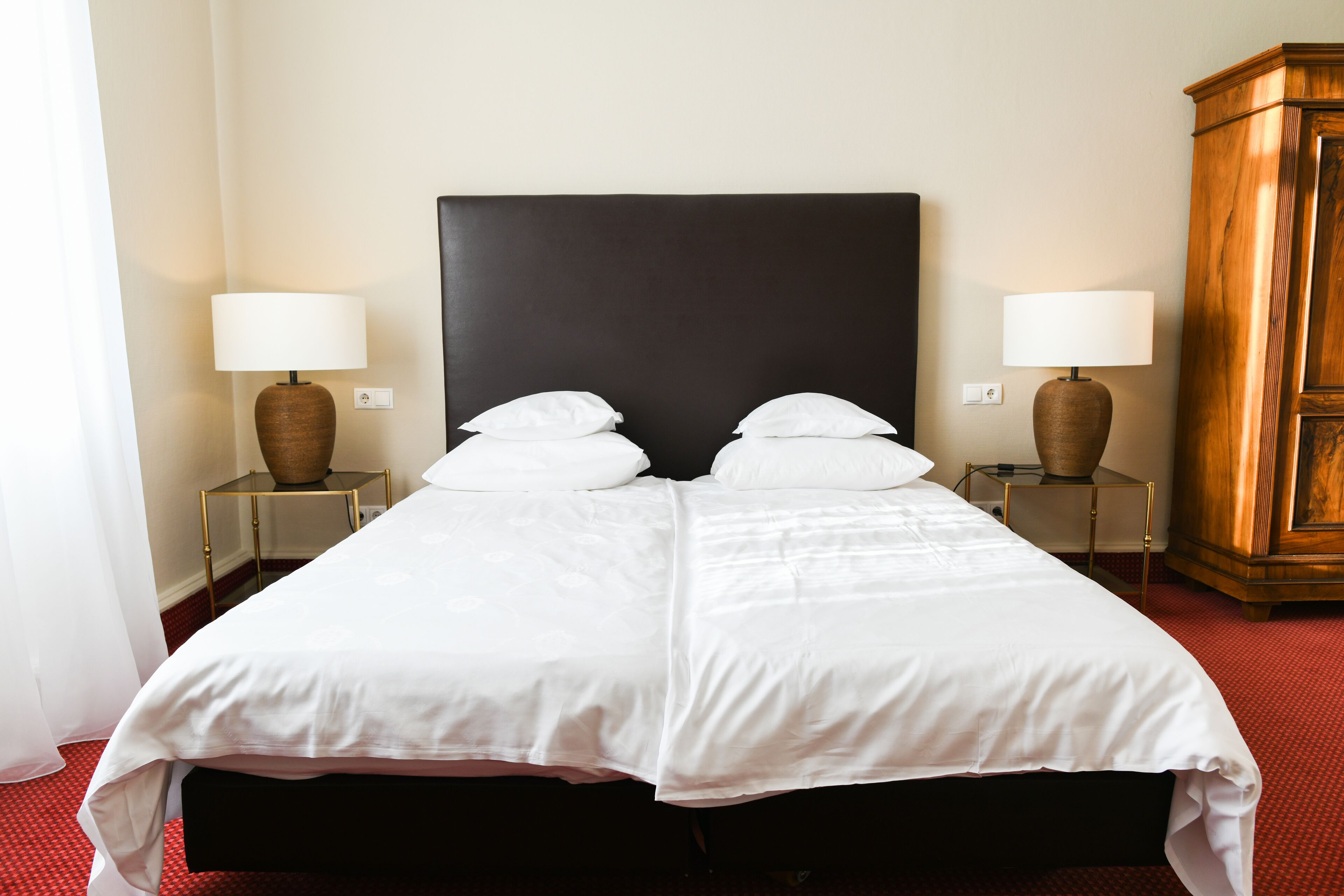 A large bed with a dark headboard, two bedside tables with lamps, and a wooden cabinet.